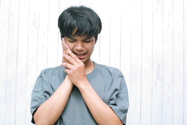 Dolor de dientes Joven que sufre de dolor de dientes fuerte y terrible con tocar la mejilla con la mano