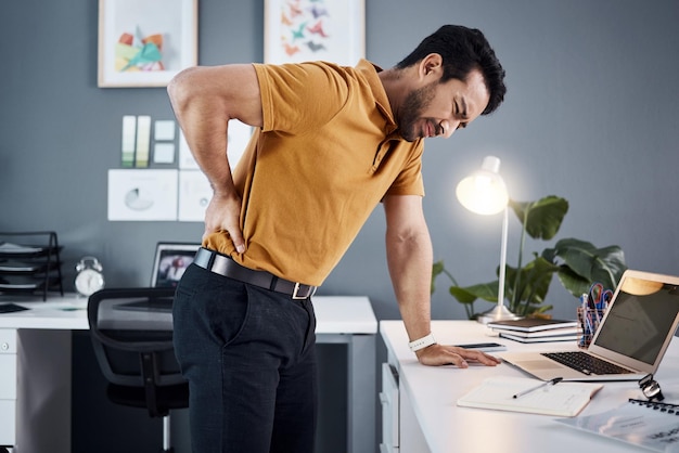 Dolor de espalda nocturno y hombre de negocios con estrés en el escritorio de la oficina en un lugar de trabajo moderno Persona profesional asiática con dolor corporal o problema de agotamiento mientras está cansado, lesionado y trabajando hasta tarde