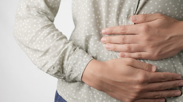 Dolor de estómago manos femeninas tocando inquietamente el vientre en primer plano de fondo blanco