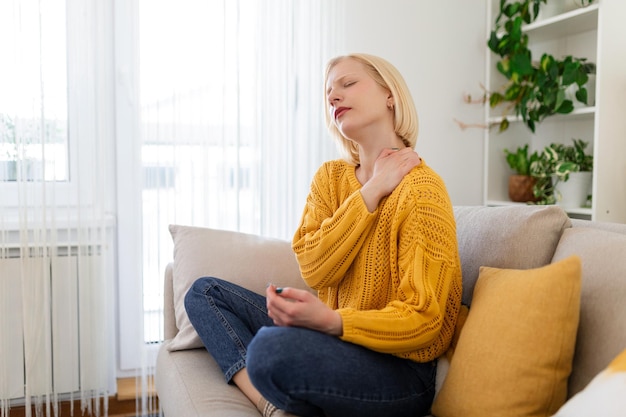 Dolor en el hombro Dolor en la parte superior del brazo Personas con problemas de músculos corporales Concepto de salud y medicina Mujer atractiva sentada en la cama y sosteniendo el hombro doloroso con otra mano