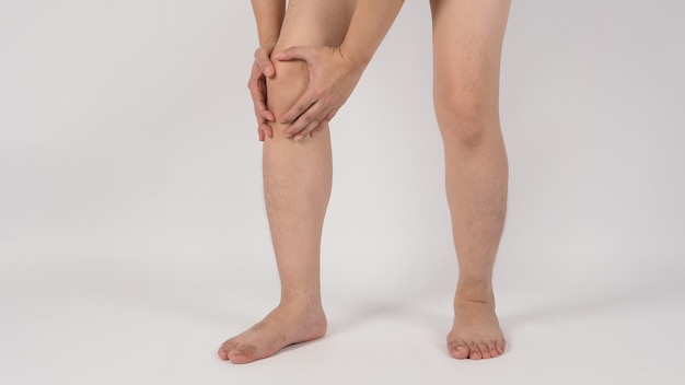 El dolor de rodilla y las piernas masculinas asiáticas y descalzo se aíslan en el fondo blanco.