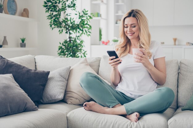 doméstica muito alegre senhora relaxando sentar sofá navegando telefone segurar caneca