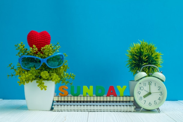 DOMINGO cartas de texto y papel de cuaderno, despertador y pequeño árbol de decoración en madera