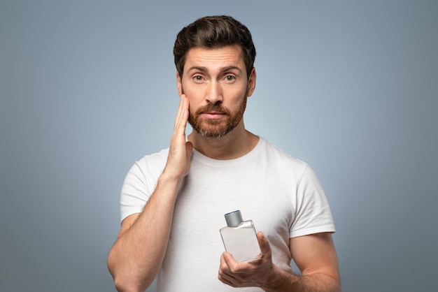 Dominio del aseo apuesto hombre caucásico de mediana edad aplicando perfume en la barba después de afeitarse gris