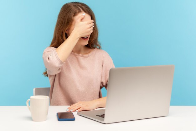 Don39t wollen sich diese verwirrte, verängstigte Frau ansehen, die ihre Augen bedeckt, und vermeiden, beschämende Inhalte auf Laptops zu sehen, die am Computer arbeiten, vom Home Office Indoor Studio Shot isoliert auf blauem Hintergrund