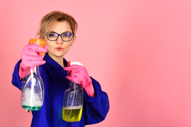 Dona de casa com material de limpeza. Serviço de limpeza e conceito de trabalho. Mulher mostra ferramentas de limpeza. Mulher com frasco de spray de limpeza. Linda garota isolada em fundo rosa. Copie o espaço para anunciar.