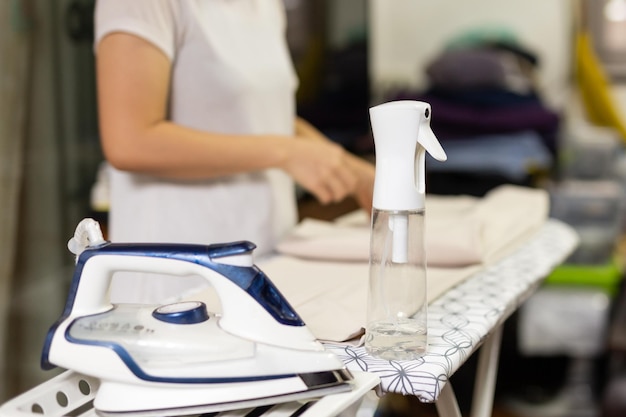 Dona de casa com spray de garrafa nebuloso para roupas de ferro na tábua de passar