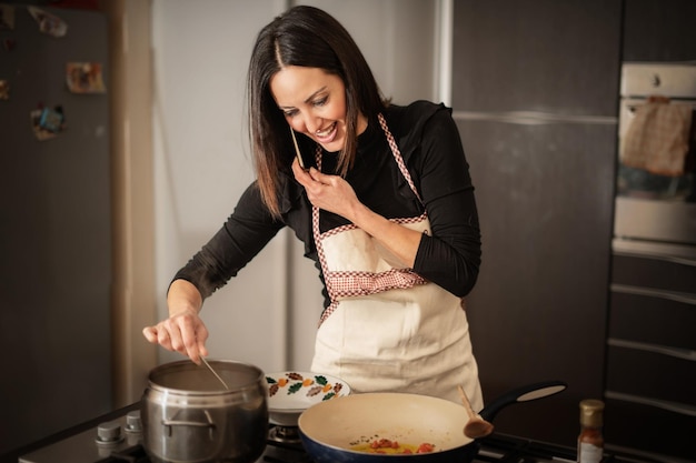 Dona de casa cozinhando enquanto tal rei ao telefone - uma mulher cozinhando e usando smartphone