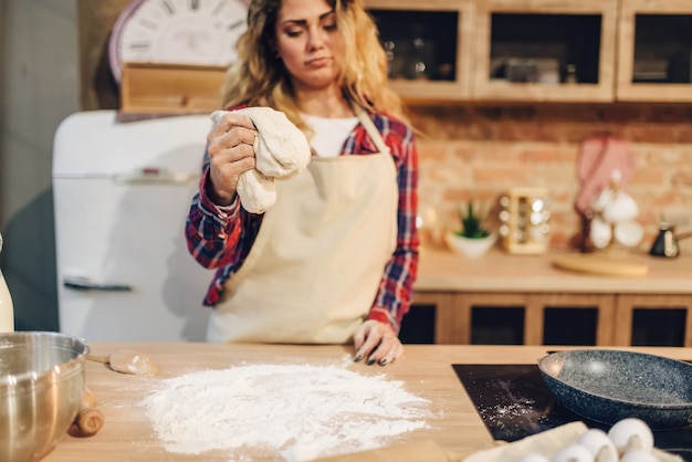 Dona de casa de avental cozinhando massa em tigela de metal