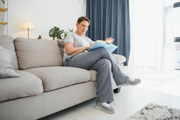 Dona de casa de meia-idade sentada no sofá com livro como hobby de aposentadoria