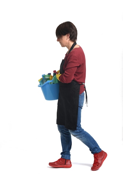 Dona de casa de retrato completo com um balde com produtos de limpeza andando sobre fundo branco