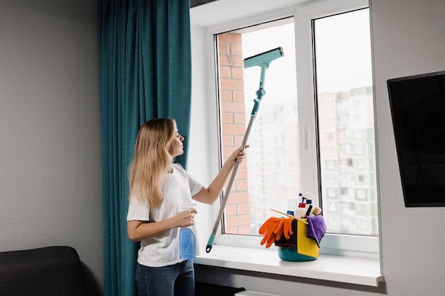 Dona de casa está limpando em casa e lavando janelas Serviço de limpeza doméstica Empregada está pulverizando detergente e limpando janelas em casa