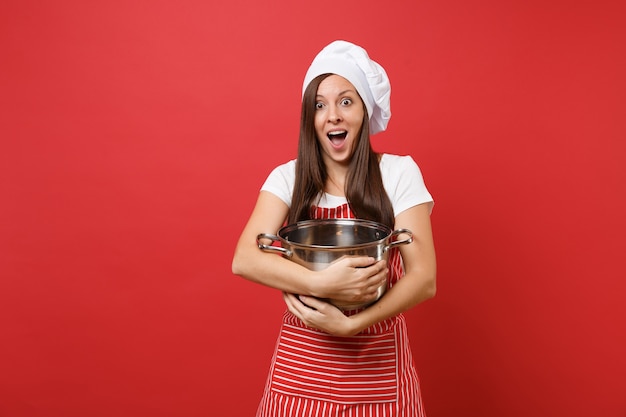 Dona de casa feminina chef cozinheira ou padeiro no chapéu de chefs avental listrado branco t-shirt toque isolado no fundo da parede vermelha. mulher linda governanta segurando o pote de louça vago. simule o conceito de espaço de cópia