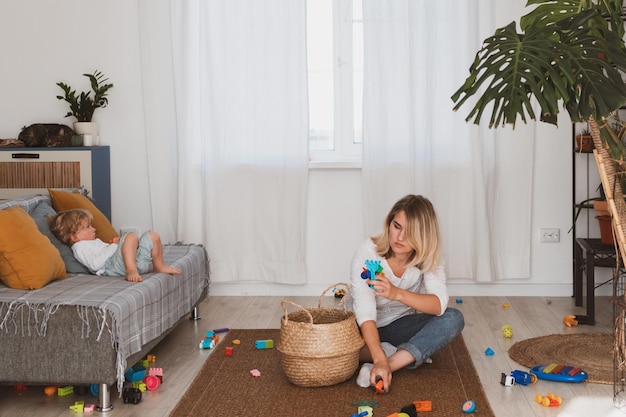 Dona de casa jovem coloca brinquedos na cesta com seu filho pequeno em casa