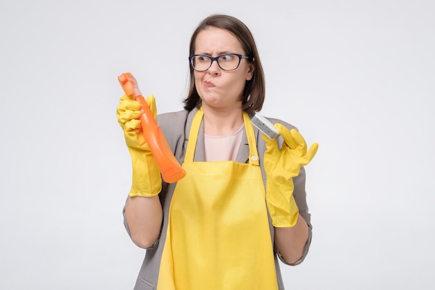 Dona de casa jovem estressada em um avental amarelo com esponja de cozinha e uma garrafa de detergente