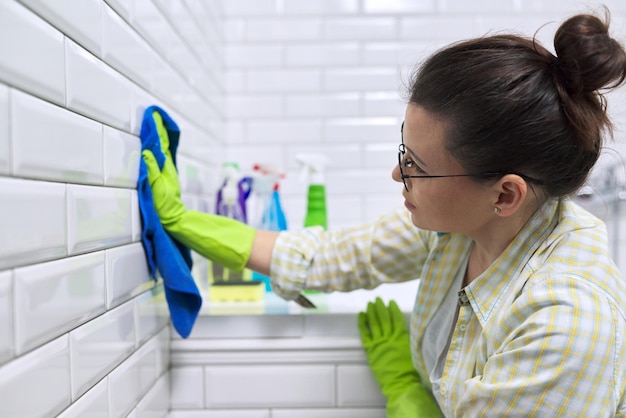 Dona de casa mulher fazendo limpeza no banheiro. parede de ladrilhos de polimento feminino no banheiro com pano de microfibra