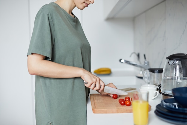 Dona de casa nova com a faca que corta tomates vermelhos na placa de madeira