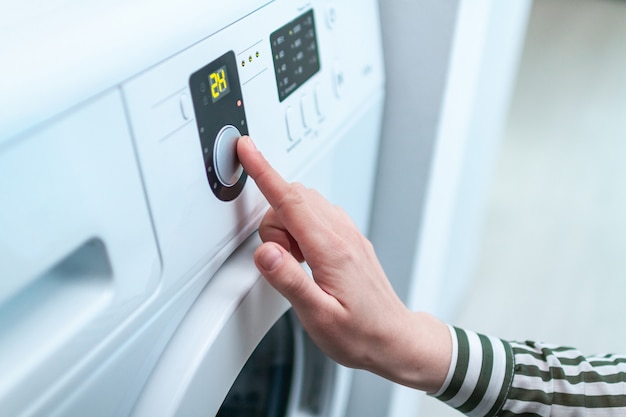 Dona de casa usando a tela e o botão para ligar e escolher o programa de ciclo na máquina de lavar para lavar roupa em casa.