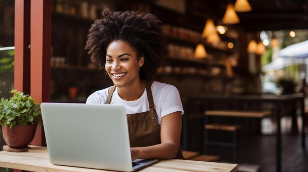 dona de uma cafeteria afro-americana em avental usando laptop na mesa do lado de fora do café