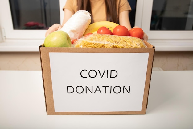 Donación de covid Atención y caridad Una niña voluntaria sostiene una caja de productos alimenticios para las personas sin hogar y los pobres