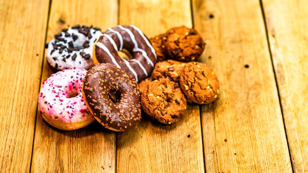 Donas y galletas coloridas en una mesa de madera Comida dulce de azúcar con salpicaduras esmaltadas Donas con glaseado de chocolate Vista superior con espacio de copia