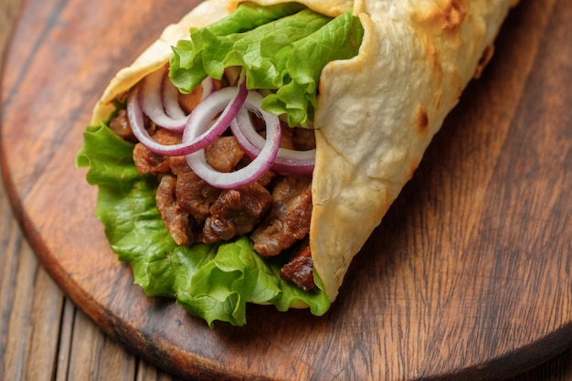 Doner kebab está acostado en la tabla de cortar. shawarma con carne, cebolla, ensalada se encuentra en una vieja mesa de madera blanca.