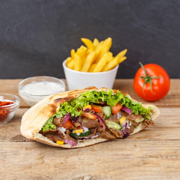 Foto doner kebab doner kebap comida rápida en pan plano con papas fritas en un tablero de madera cuadrado