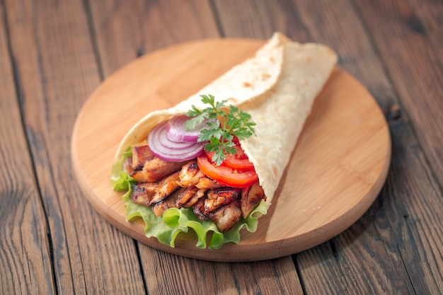 Doner kebab está acostado en la tabla de cortar. Shawarma con carne de pollo, cebolla, ensalada se encuentra en una vieja mesa de madera oscura.