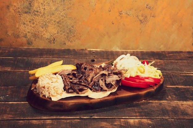Doner kebab está acostado en la tabla de cortar Shawarma con ensalada de cebollas de carne yace en una madera oscura y vieja