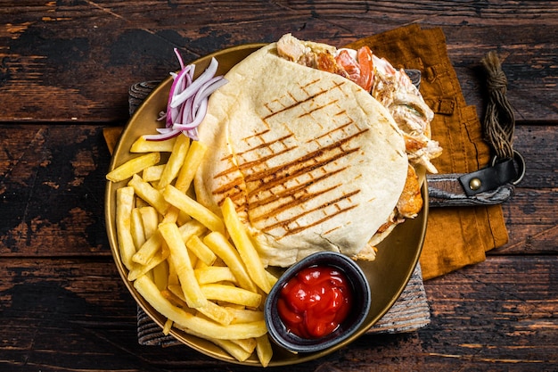 Doner kebab Shawarma en pan de pita a la parrilla con carne de verduras y papas fritas Fondo de madera Vista superior