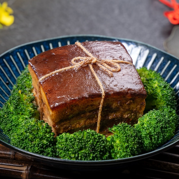 Dong Po Rou (carne de cerdo Dongpo) en un hermoso plato azul con verduras de brócoli verde, comida festiva tradicional para la comida de la cocina del año nuevo chino, de cerca.