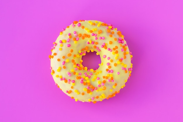 Donut amarillo esmaltado sobre fondo rosa brillante.