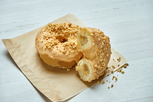 Donut apetitoso con glaseado amarillo y relleno de maní sobre papel artesanal en una mesa de madera. Cortar la rosquilla. Postre americano clásico