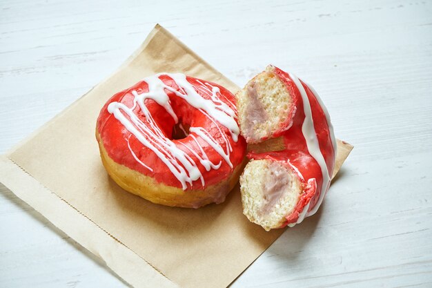 Donut apetitoso con glaseado rojo y relleno de cereza sobre papel artesanal en una mesa de madera. Cortar la rosquilla. Postre americano clásico