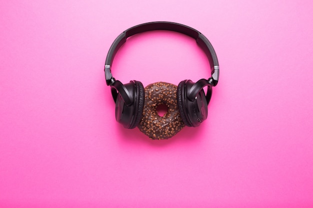 Foto donut y auriculares sobre un fondo rosa. concepto de almuerzo de negocios y descanso después del trabajo.