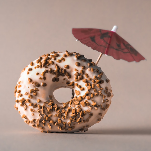 Donut aus weißer Schokolade mit Mandeln und einem Dekorationsschirm auf grauem Hintergrund