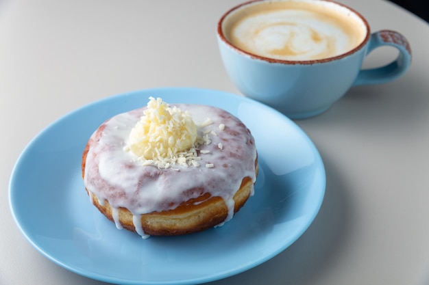 Donut bedeckt mit Puderzucker und Kokoschips auf blauem Teller und Tasse Cappuccino