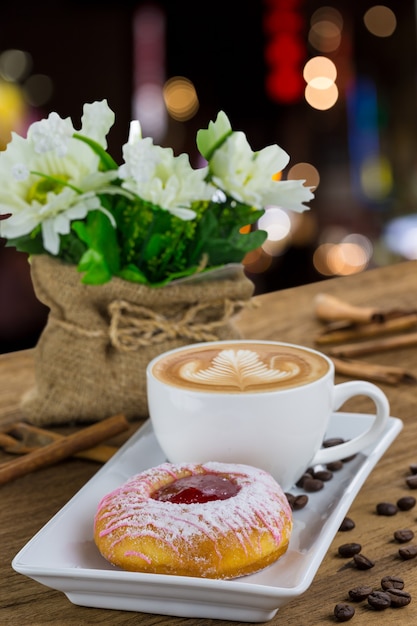 Donut y café con leche en plato blanco sobre mesa de madera