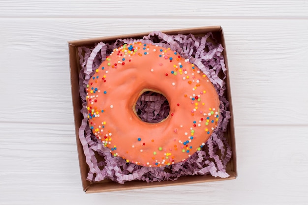 Donut en caja sobre fondo blanco de madera. Caja con pastel de naranja sobre mesa de madera.