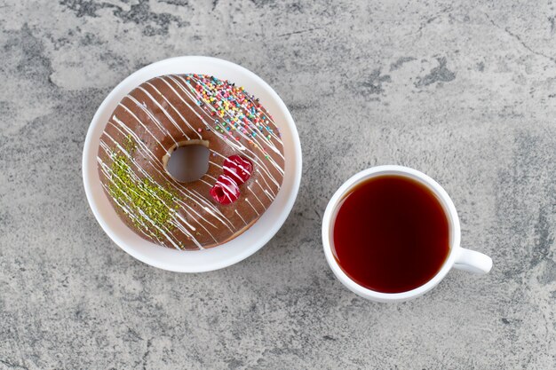 Donut de chocolate con bayas y chispitas y taza de té caliente sobre fondo de piedra.