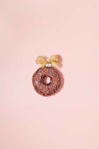 Donut de chocolate con lazo dorado sobre fondo rosa vista superior de una sola bola acristalada