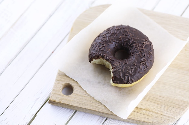 Donut de chocolate sobre un fondo blanco de madera y una dispersión de adornos dulces