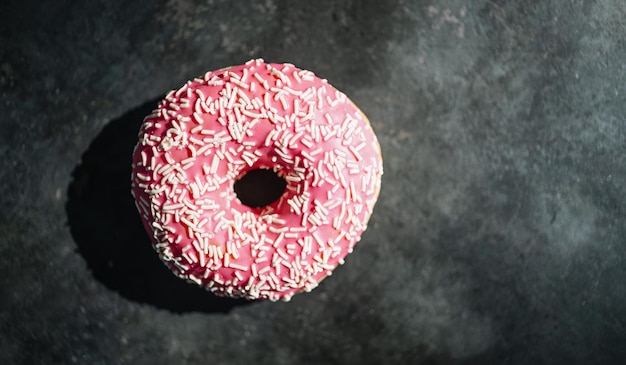 Donut com esmalte rosa e granulado em uma mesa escura