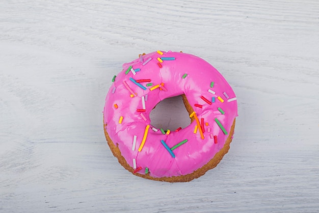 Donut com esmalte rosa sobre fundo branco de madeira