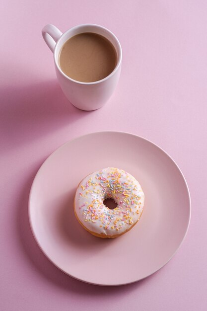 Donut de baunilha com granulado no prato perto de xícara de café, comida de sobremesa vitrificada doce e bebida quente no fundo rosa mínimo, vista de ângulo