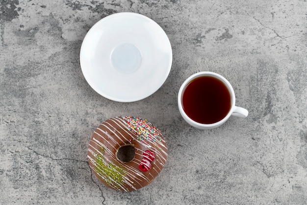 Donut de chocolate com frutas e granulado e uma xícara de chá quente no fundo de pedra.