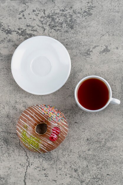 Donut de chocolate com frutas e granulado e uma xícara de chá quente no fundo de pedra.