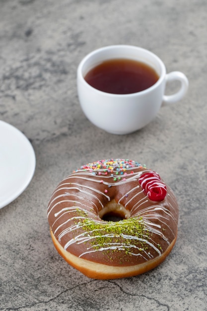 Donut de chocolate com frutas e granulado e uma xícara de chá quente no fundo de pedra.