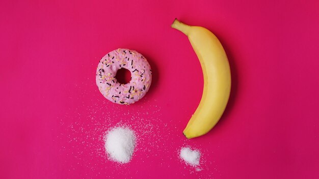 Donut de escolha contra banana - açúcar e calorias nos alimentos. começar uma alimentação saudável ou junk food. fundo rosa