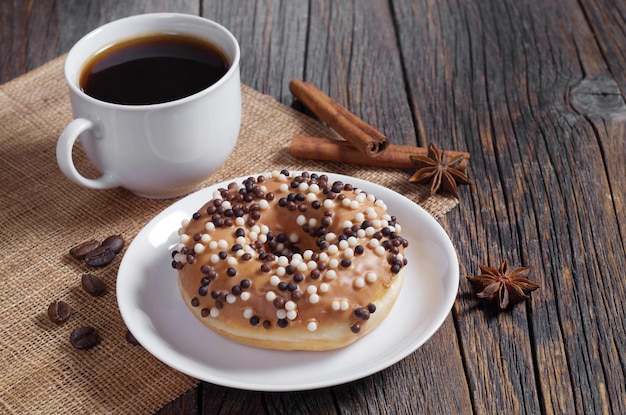 Donut decorado com bolas de chocolate preto e branco no prato e xícara de café na velha mesa de madeira